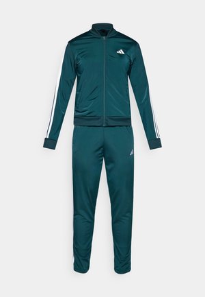 Completo atletico di un verde scuro in tessuto liscio, composto da giacca con zip e strisce bianche sulle maniche e pantaloni coordinati.