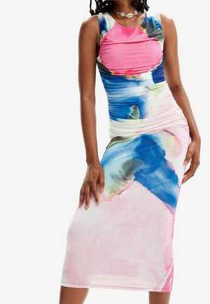 Kobieta ubrana w sukienkę bez rękawów z marszczeniami, w abstrakcyjne wzory tie-dye w kolorach niebieskim, różowym i białym oraz z naszyjnikiem z muszelek.