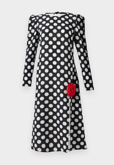 Musta mekko, jossa on valkoisia pilkkuja, pitkät hihat ja frilla kauluksessa. Edessä helmaosassa on punainen ruusuyskä.