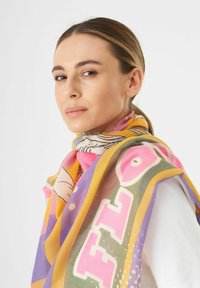 Écharpe multicolore présentant des teintes roses, jaunes et vertes avec de bold motifs graphiques et une texture douce, drapée de manière décontractée autour du cou du modèle.