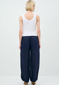 Top bianco senza maniche abbinato a pantaloni leggeri e larghi di colore blu navy, caratterizzati da un tessuto testurizzato e dettagli con cordoncino sui polsini.