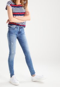 Jeans ajustados azules con detalles desgastados, combinados con una camiseta de manga corta a rayas en rojo, blanco y azul marino. Zapatillas blancas completan el look.