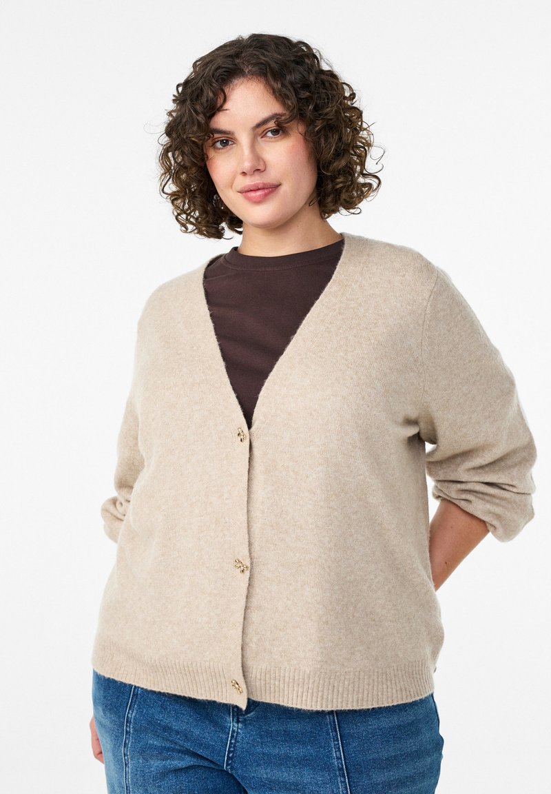 Kafijas krāsas kardigāns ar v-veida kakla izgriezumu, zelta krāsas pogām un ribinātu apakš malā. Mīksta tekstūra, garas piedurknes, valkāts virs tumši brūna krekla.