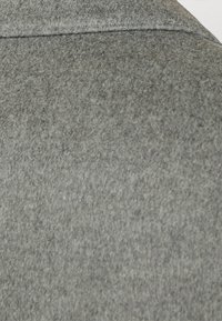 Materiale di lana grigia con una superficie testurizzata, caratterizzato da una cucitura liscia nella parte superiore, che indica un design di abbigliamento strutturato.