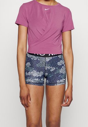 Person trägt ein kurzärmeliges, pinkes Nike Crop-Top und dunkelblaue Sportshorts mit Blumenmuster und einem schwarzen Bund.