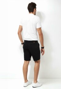 Black shorts with a smooth texture and a casual design, paired with a plain white short-sleeve t-shirt and white sneakers.