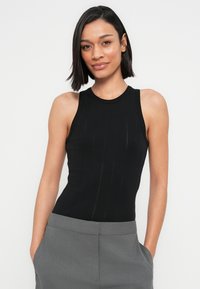 Μαύρο αμάνικο τοπ με εφαρμοστή γραμμή, διακοσμημένο με διακριτικά κάθετα ριμπ λεπτομέρειες. Συνδυάζεται με γκρι παντελόνι ψηλόμεσο.