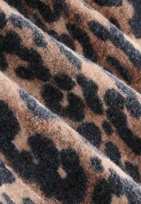 Tissu imprimé léopard dans des tons de beige et de noir. Texture douce avec un aspect pelucheux ; des taches irrégulières créent un motif audacieux.