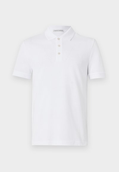 Bílá polo košile z bavlny, s dvouknoflíkovým zapínáním, krátkými rukávy a jemným logem na hrudi. Hladká textura.