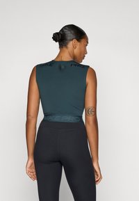 Top sportiv fără mâneci de culoare verde închis, cu un spate texturat, având sigla "NIKE PRO". Asortat cu colanți negri cu talie înaltă.