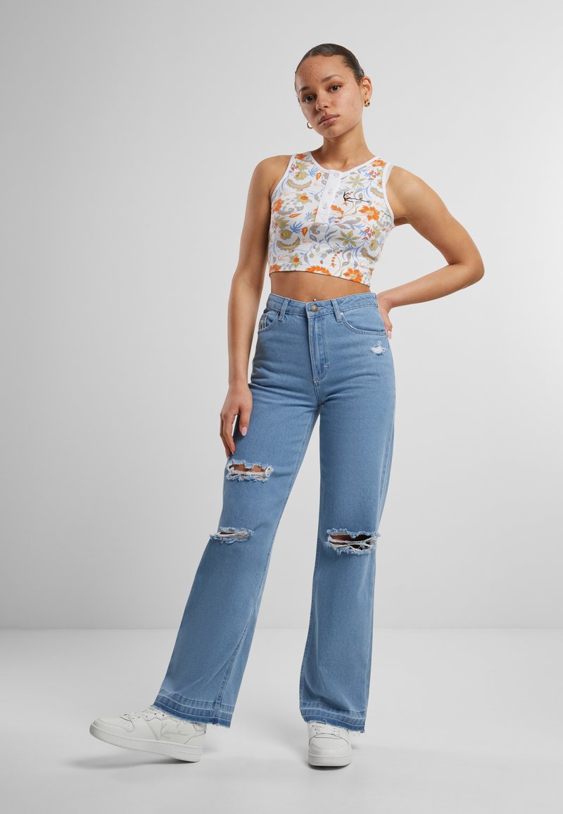 Zastrihnutý biely tielko s kvetinovým vzorom, skombinované so svetlomodrými džínami s vysokým pásom, ktoré majú poškodené otvory, a bielymi teniskami.