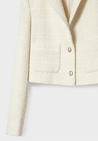 Blazer en bouclé texturé crème avec manches longues, deux poches avant et deux boutons ronds dorés à l'avant.