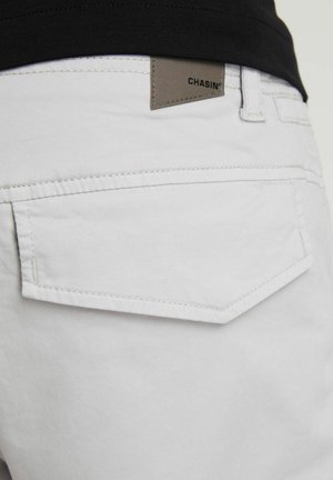 Lys grå bomuldsbukser med en baglomme i diamantform og et brunt lædermærke med teksten "CHASIN'".