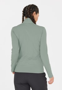 Lys grøn langærmet bluse med høj krave. Glat tekstur, tætsiddende design og sømme langs ærmerne og kanten. Minimalistisk stil.