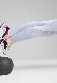 Vita leggings med spetsmönstrade paneler längs sidorna, tillsammans med svartvita sportskor med rosa detaljer, vilande på en vikt.