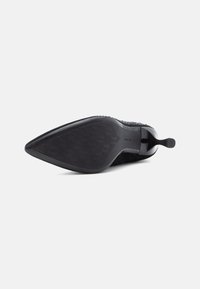 Sapato de salto alto preto com bico fino, parte superior texturizada e acabamento suave na sola. Apresenta um salto stiletto esguio.