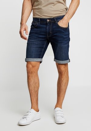 Dunkelblaue Denim-Shorts im klassischen Schnitt, mit umgeschlagenen Säumen, Fünf-Taschen-Design und einem sauberen Finish, kombiniert mit weißen Sneakers.