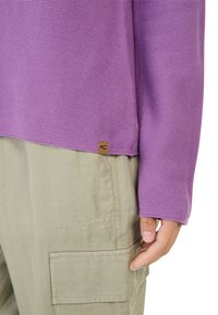 Lilla strikket top med lange ærmer og ribbet tekstur, parret med lyse khaki cargo bukser med en sidelomme. Brun tag-detalje ved kanten.
