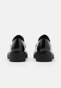 Paire de chaussures en cuir noir brillant avec semelles épaisses, vues de dos sur un fond blanc uni.