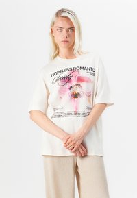 Krämbelagd bomull t-shirt med korta ärmar, med en rosa orkidé-grafik och texten: "HOPPLÖST ROMANTISK Sällskap" på framsidan.
