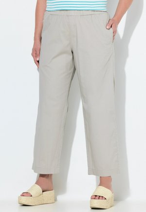 Pantalons beige à jambes larges avec ceinture élastique portés par une personne debout, associés à des sandales à plateforme tissées et un haut rayé partiellement visible.
