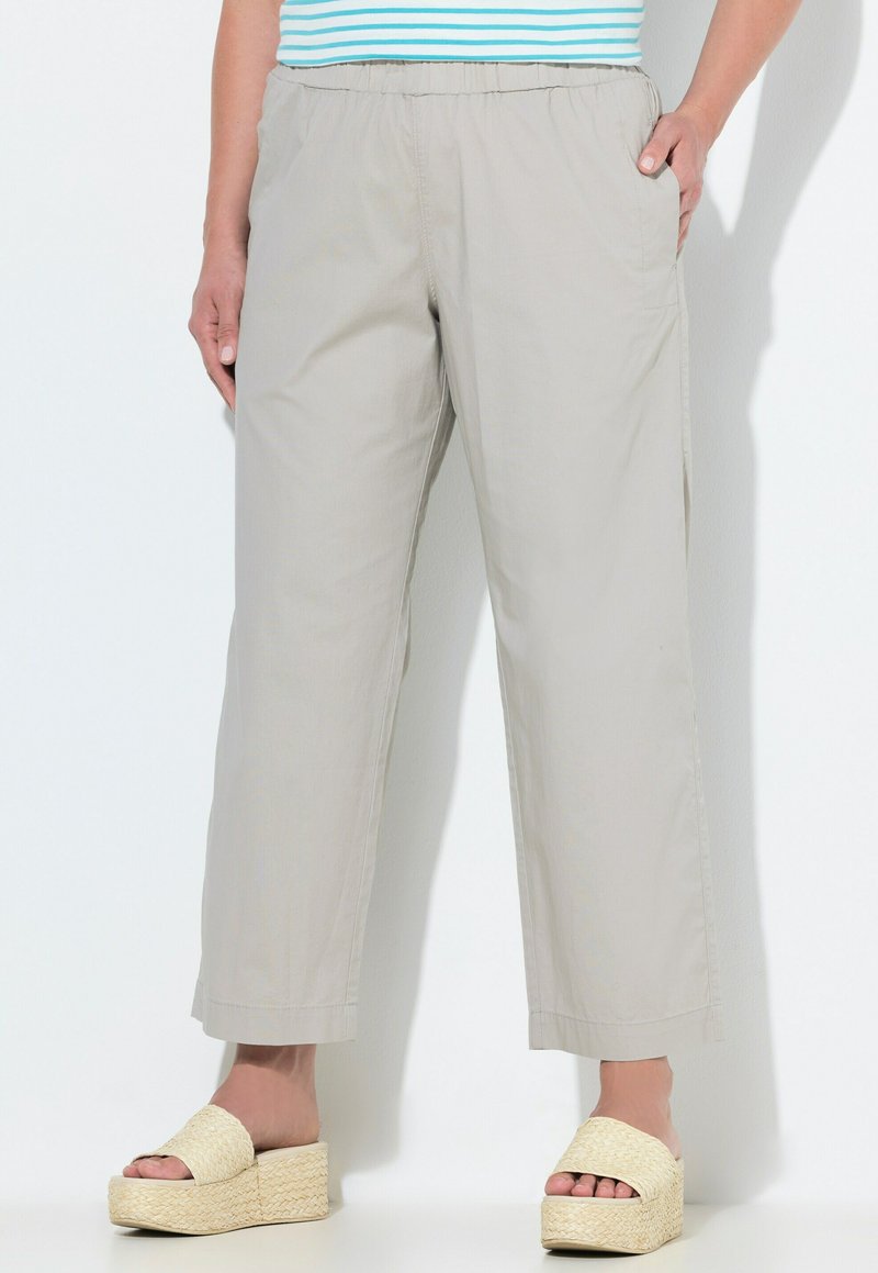 Pantalons beige à jambes larges avec ceinture élastique portés par une personne debout, associés à des sandales à plateforme tissées et un haut rayé partiellement visible.
