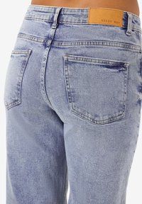 Τζιν παντελόνι σε ανοιχτό μπλε χρώμα με ψηλή μέση, που διαθέτει δερμάτινη ετικέτα με την ένδειξη "NOISY MAY" και δύο πίσω τσέπες. Διακριτικές λεπτομέρειες από φθορά.