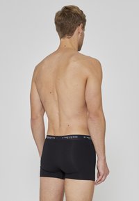 Schwarze Boxershorts mit einem weichen Bund, der den Markennamen trägt. Der Stoff wirkt glatt und eng anliegend. Rückansicht zeigt ein schlichtes Design.
