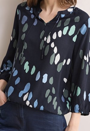 Blusa navy con scollatura a V, caratterizzata da dettagli con coulisse e una vestibilità morbida. Decorata con motivi a forma di foglia in diverse tonalità di blu e verde.