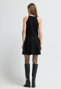 Zwart mouwloos jurk met een wijde rok, gemaakt van een gladde stof. Gepaard met zwarte leren laarzen tot de knie met gouden accenten.