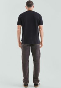 Schwarzes Baumwoll-T-Shirt mit kurzen Ärmeln, kombiniert mit dunkelgrauen Hosen. Das Outfit zeichnet sich durch eine lockere Passform und ein minimalistisches Design aus.