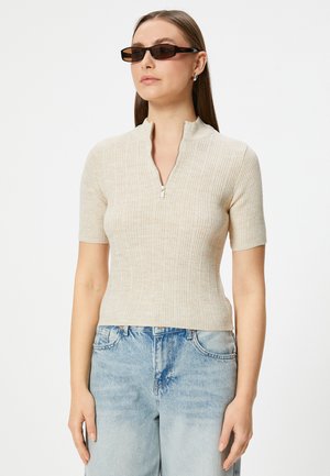 Beige ribbed knit top with a half-zip collar and short sleeves, paired with light blue denim jeans. The fabric appears soft and textured.