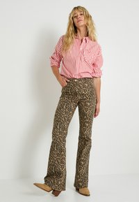 Camisa de botones a rayas rojas y blancas con un bolsillo en el pecho, combinada con pantalones acampanados de leopardo marrón y botas de tacón beige.