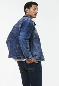 Blå denimjacka med en något urblekt finish, med klassisk design, knappstängning och fickor, i kombination med mörka jeans.