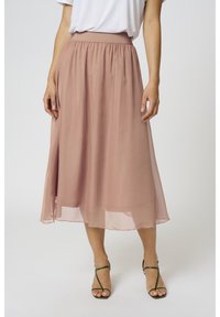 En lång, flödande kjol i mjuk, rosig chiffon med elastisk midja och lagerdesign, kombinerad med gröna sandaletter med remmar.