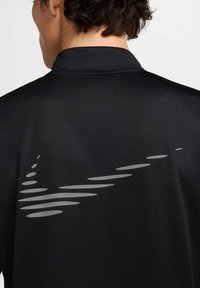 Henkilö, jolla on musta paita, jossa on takana harmaa Nike-swoosh, joka on tyylitelty pitkulaisista ovaalinmuotoisista paloista, kuvattuna takaa.