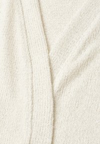 Gros plan d'un tissu tricoté doux de couleur crème avec un motif côtelé subtil et de fins détails de texture.