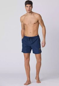 Costumi da bagno blu con vita elastica e cordoncino, dotati di un piccolo logo ricamato, lunghi fino al ginocchio, realizzati in tessuto leggero.