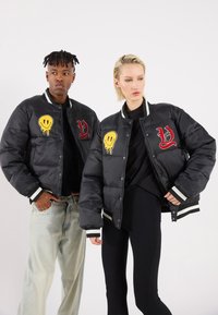 Black padded jackets with embroidered yellow smiley and red letters. Each has striped accents on the collar and cuffs. Casual fit.