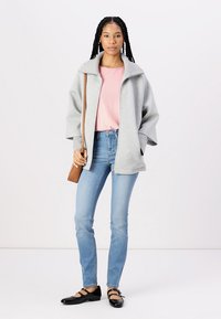 Lys grå glidelåsjakke med høy krage, båret over en rosa stripete topp. Lyseblå smale jeans og svarte flate sko med stropper.