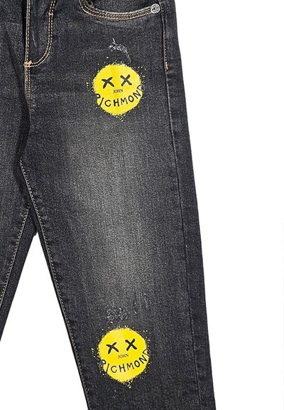 Jeans in denim nero con toppe strappate e design di faccine sorridenti gialle. Segni di usura visibili sulla texture del tessuto.