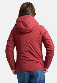 Giacca isolante rossa con cappuccio, caratterizzata da una texture liscia, design aderente e dettagli delle cuciture; abbinata a jeans blu.