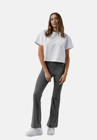 Przycięta biała koszulka z krótkim rękawem, zestawiona z szarymi spodniami dzwonami. Obuwie to białe trampki. Prosty i swobodny design.