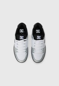 Zapatillas de la marca DC en blanco y plata con forro interior y cordones negros, vistas desde arriba sobre un fondo blanco liso.