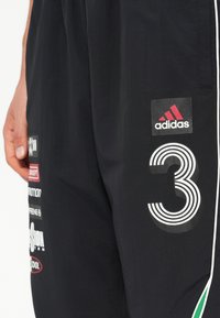 Melni sporta bikses ar baltām svītrām, lielu "3" grafiku un vairākiem zīmola logotipiem. Audums izskatās viegls un gluds.
