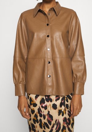 Chemise boutonnée en fausse cuir marron avec manches longues bouffantes, associée à une jupe beige ornée d'un imprimé léopard abstrait noir et marron.