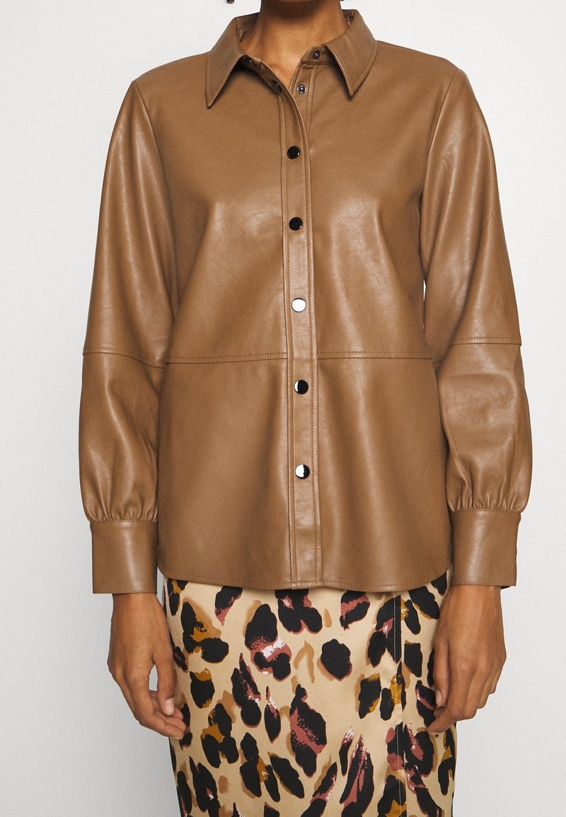 Chemise boutonnée en fausse cuir marron avec manches longues bouffantes, associée à une jupe beige ornée d'un imprimé léopard abstrait noir et marron.