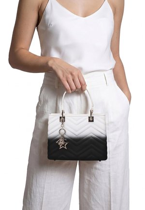 Vrouw in witte outfit met een kleine zwart-witte getailleerde gewatteerde handtas met zilveren bedels in de vorm van sterren.