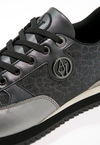 Svart och grå sneaker med en mjuk läder- och textilöverdel, runda skosnören, en cirkulär logotypdetalj och en gummisul.