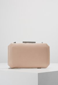 Beige rektangulär clutchväska med rundade hörn, silverfärgad metallspänne och kedjearm hållande på en vit yta.